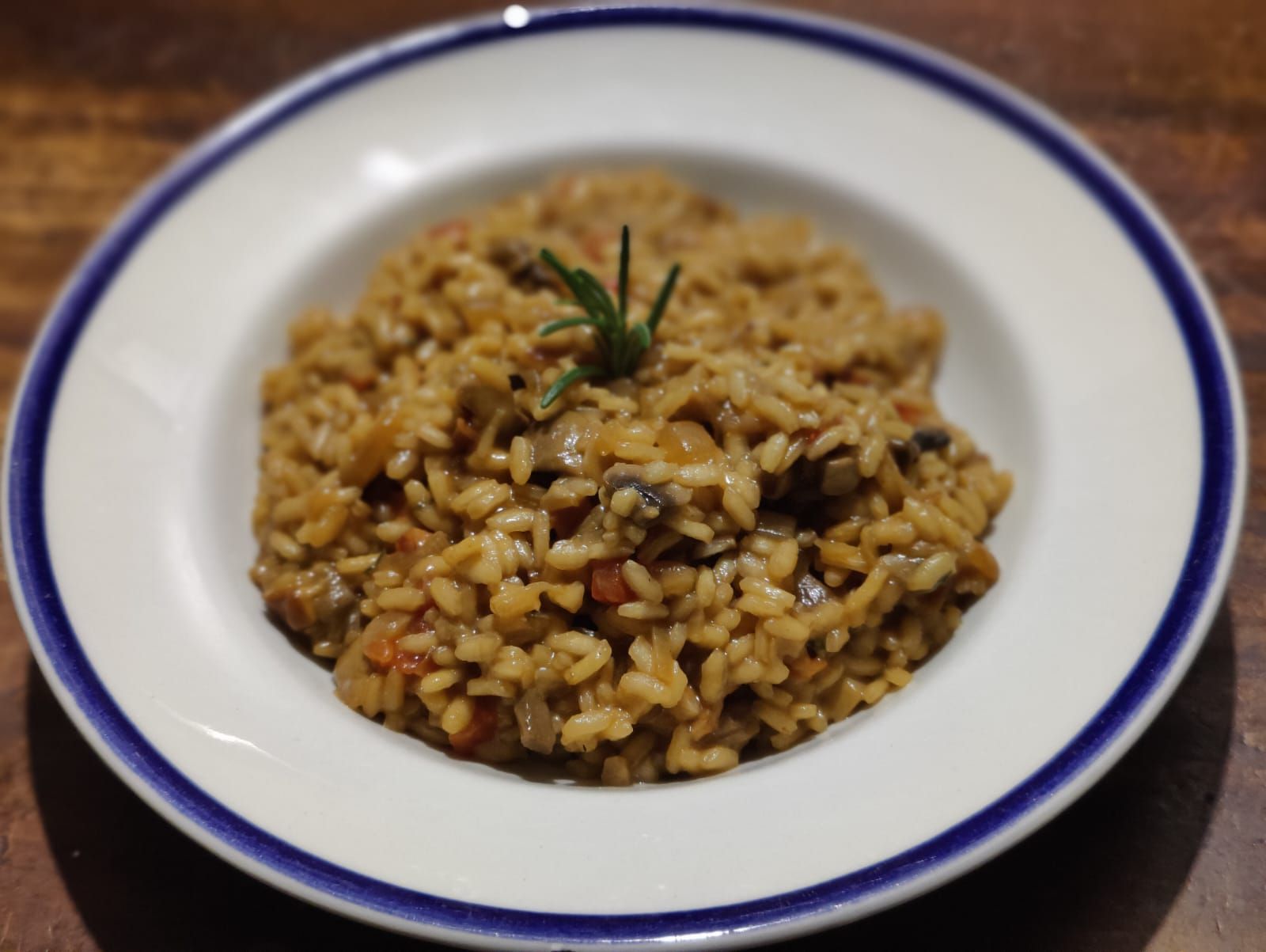 Creamy porcini risotto with diced veggies and rosemary on a white plate with a blue rim.