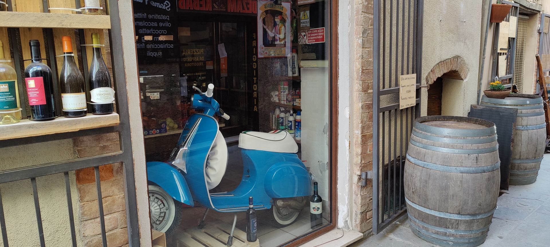 Vintage blue vespa displayed in wine shop window in a narrow cobblestone alley with barrels