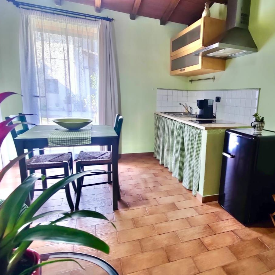 Bedroom with sloped wooden ceiling, king bed with quilt and white pillows between lit shelves, wardrobe by curtained window, tiled floor.