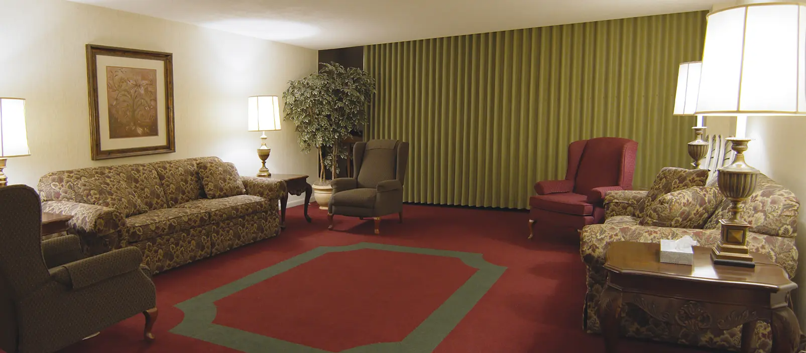 A living room with floral sofas, a red rug, green curtains, and warm lighting.