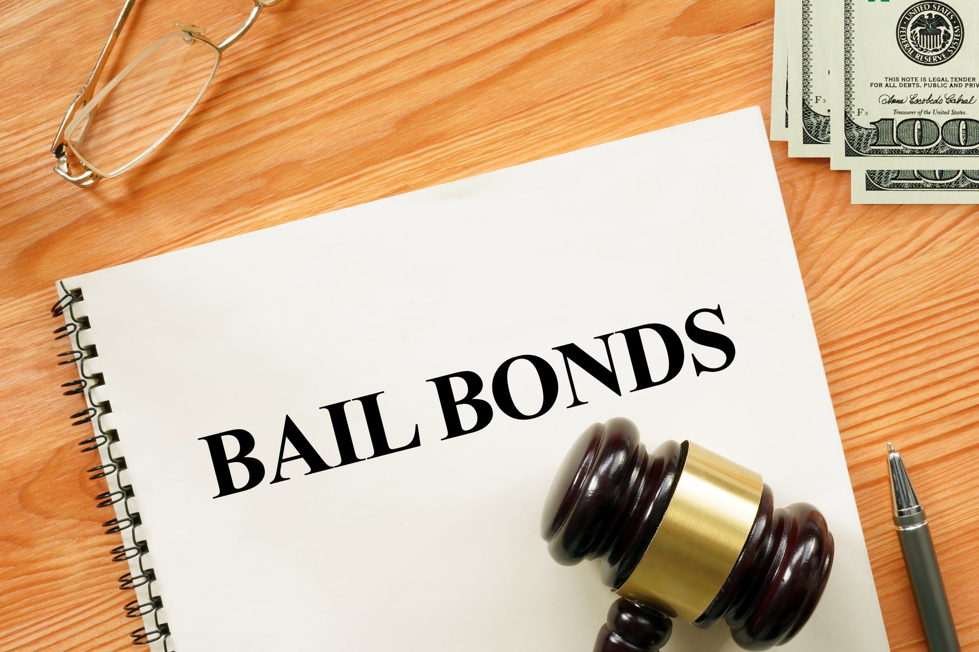 Bail bonds paperwork rests beside gavel, pen, and cash pile on polished wooden desk.