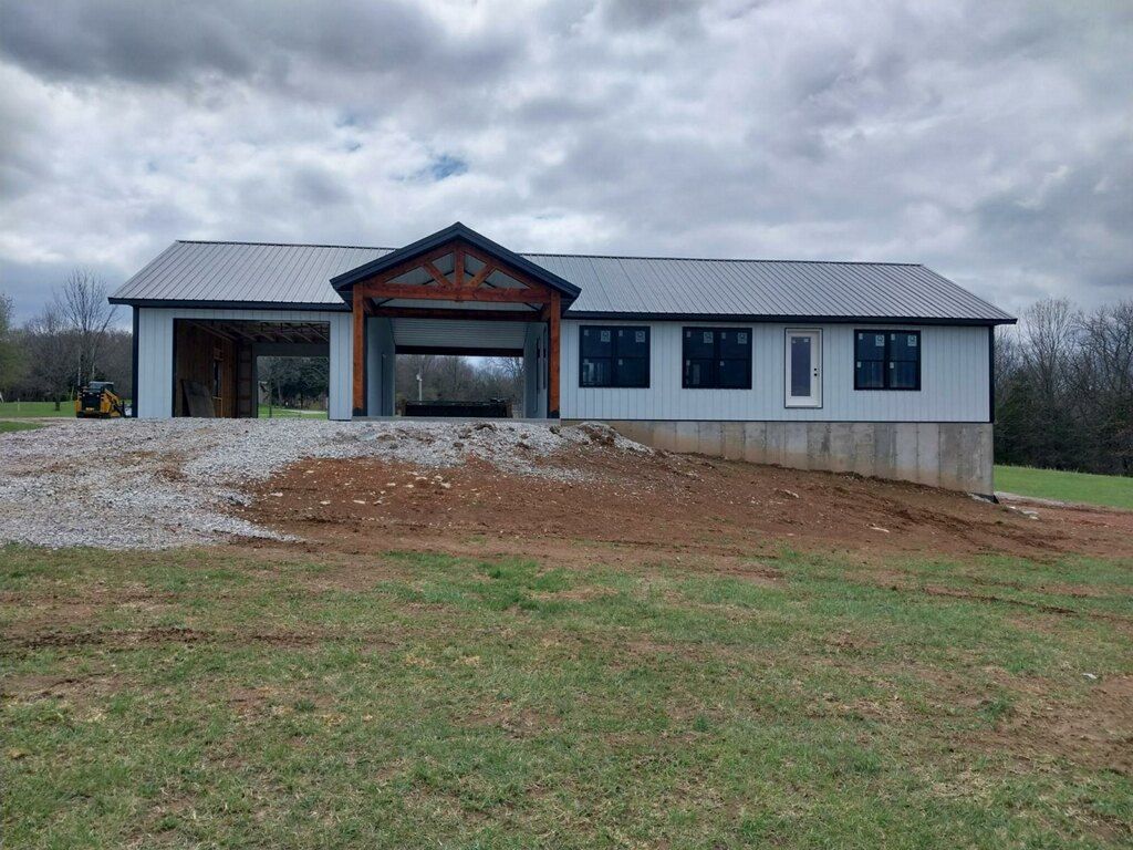 New house under construction with gray siding, metal roof, and garage doors open to the outside.