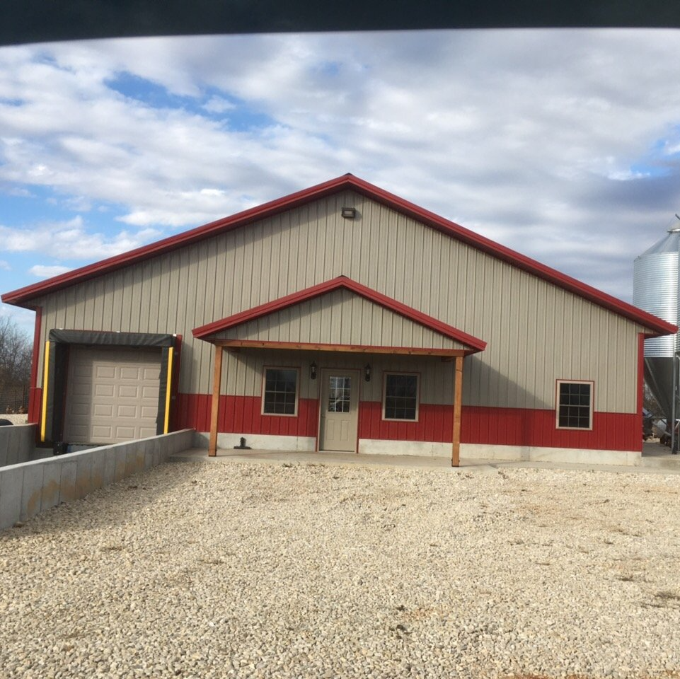 Beige and red metal building with gravel lot under a cloudy sky.