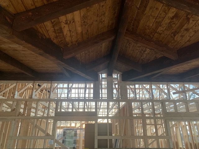 Interior view of unfinished wooden house under construction; exposed beams, light-filled windows and framing.