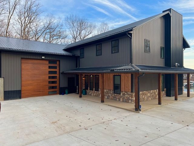 Modern dark gray house with wood accents, garage door, and stone base, against a blue sky.
