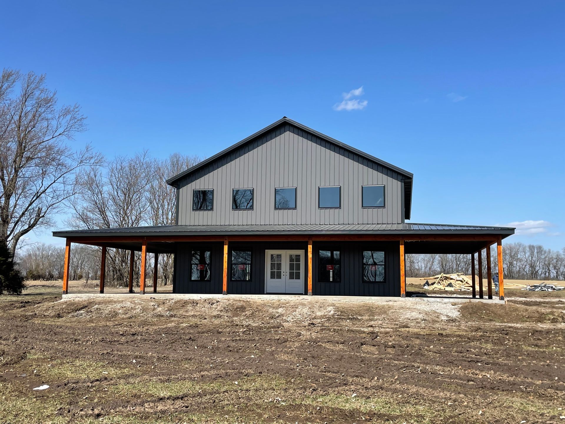 Gray barn-style house with porch, windows, and a blue sky.