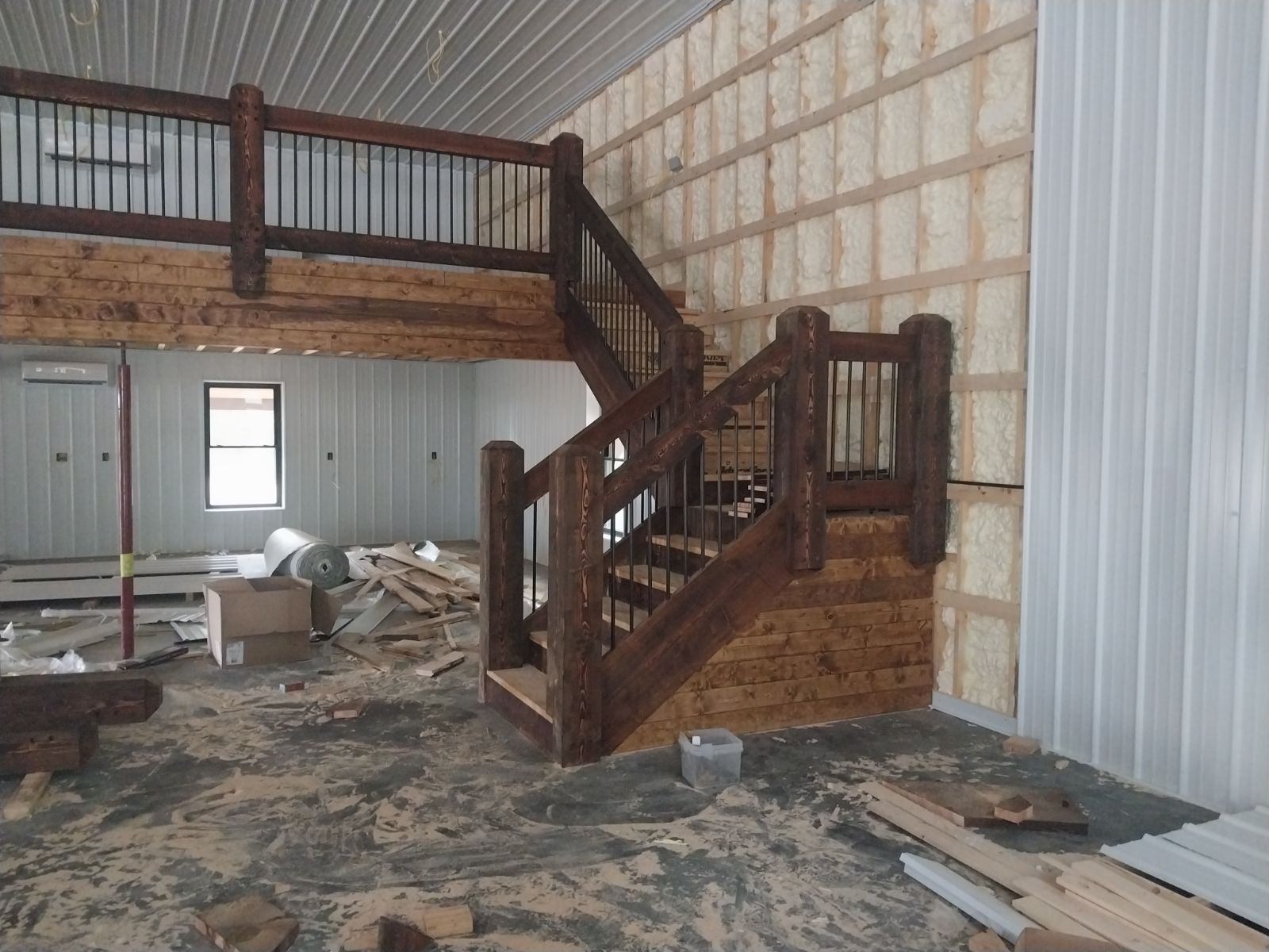 Interior shot: wooden staircase with log accents leading to a loft in a partially constructed building.
