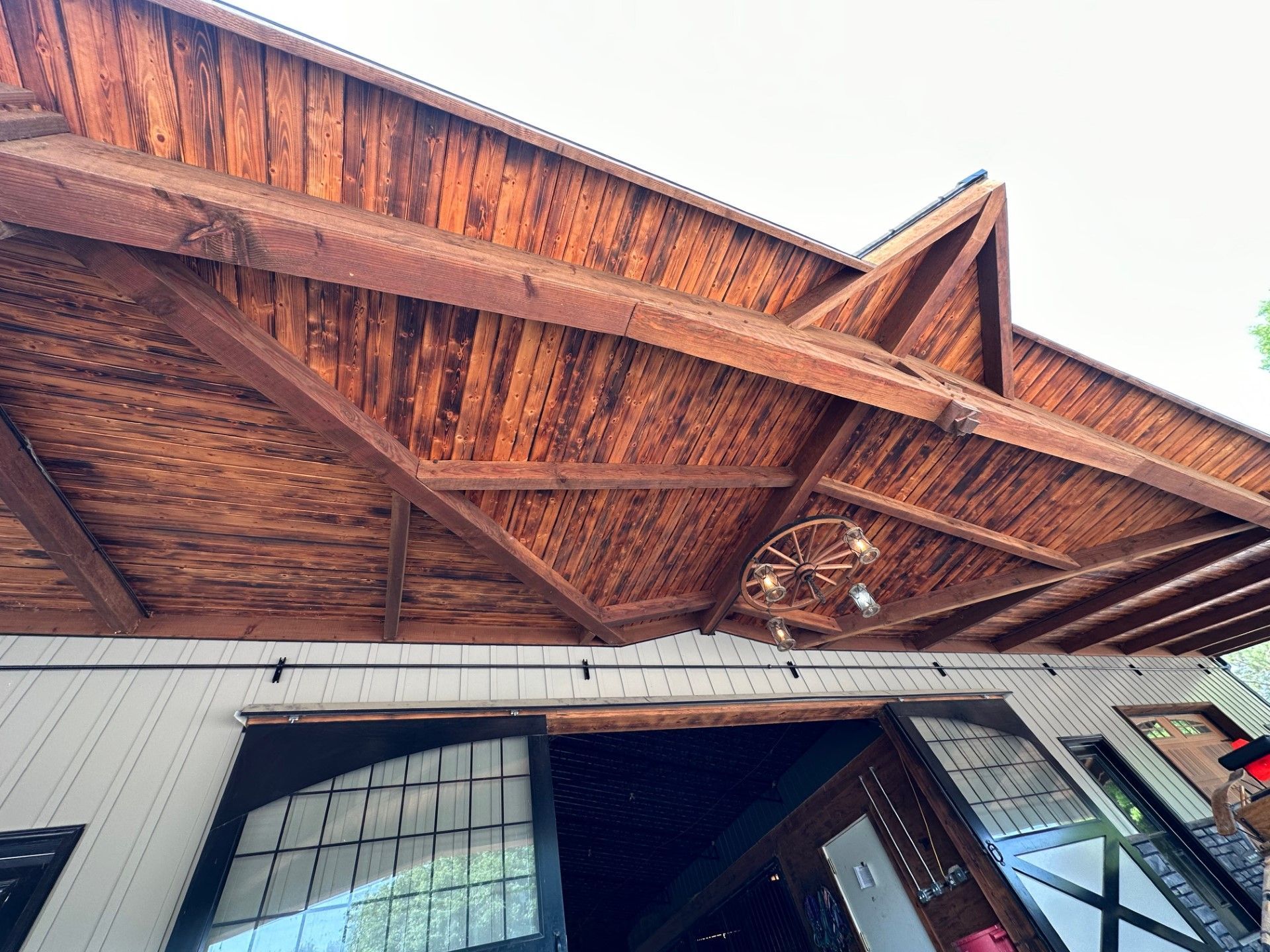 Wooden ceiling over a building with sliding doors; a wagon wheel-shaped chandelier hangs.