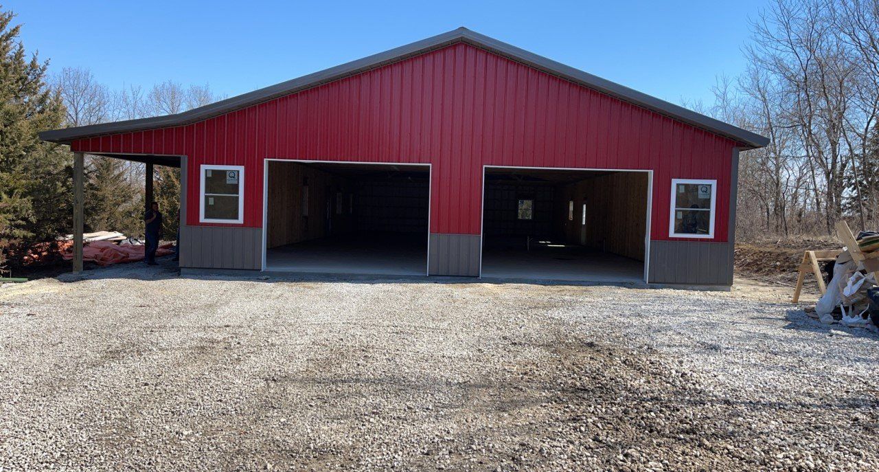 Red and gray metal garage with two open bays and a gravel driveway.
