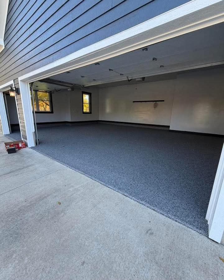 Open garage with a dark speckled floor, light walls, and a blue siding exterior.