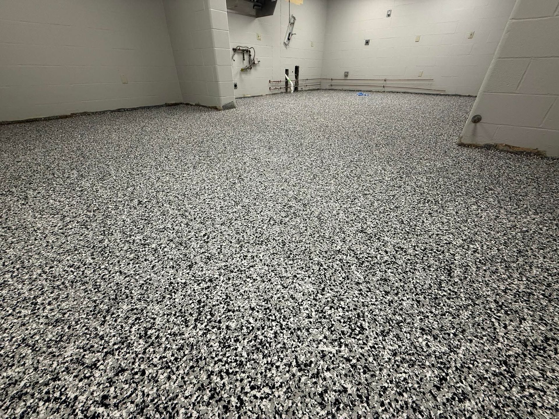 Person using a spiked roller on a shiny, light-colored floor; indoor, construction setting.