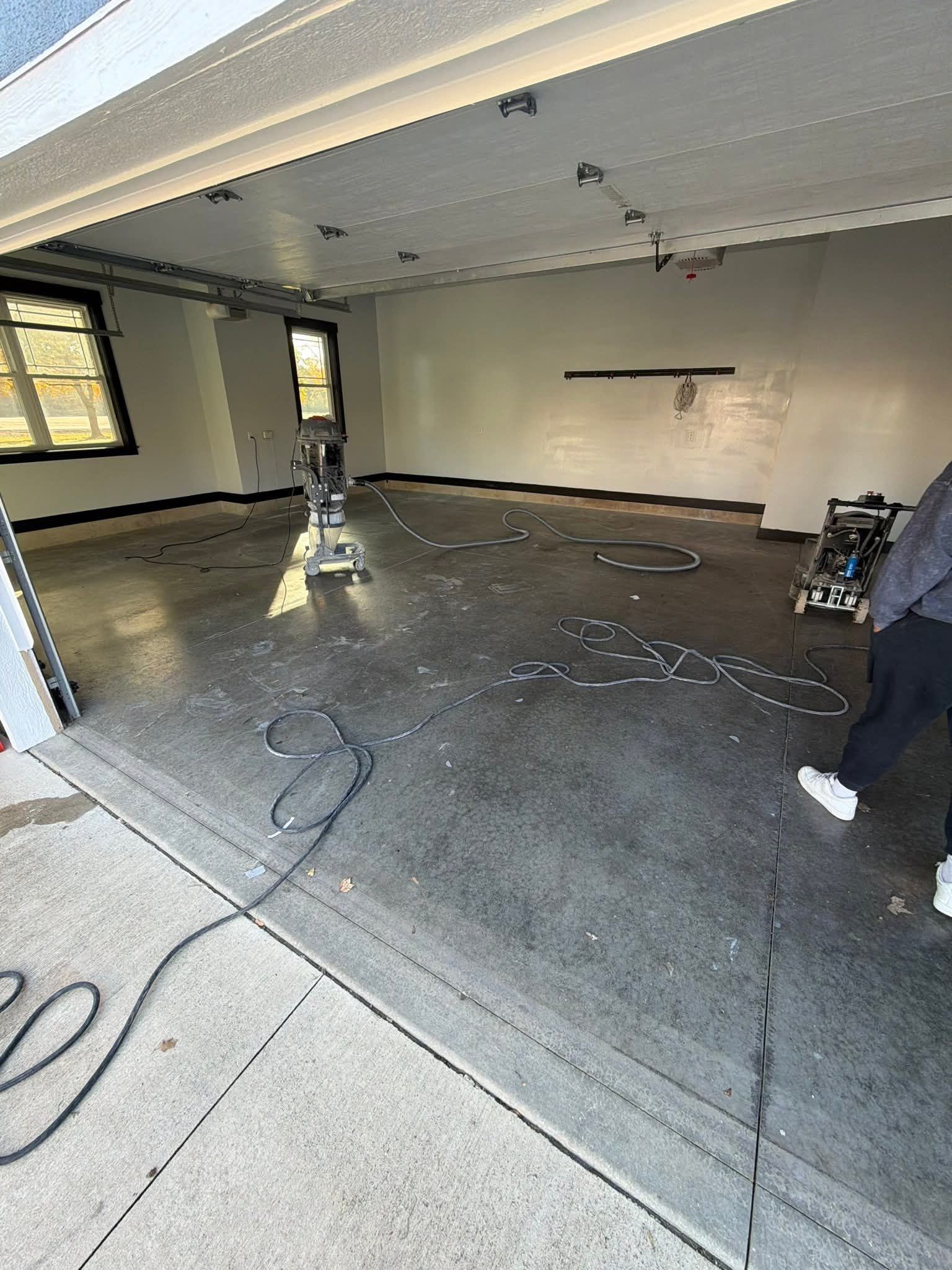 Garage interior, concrete floor being cleaned. Two workers, machines and hoses visible.