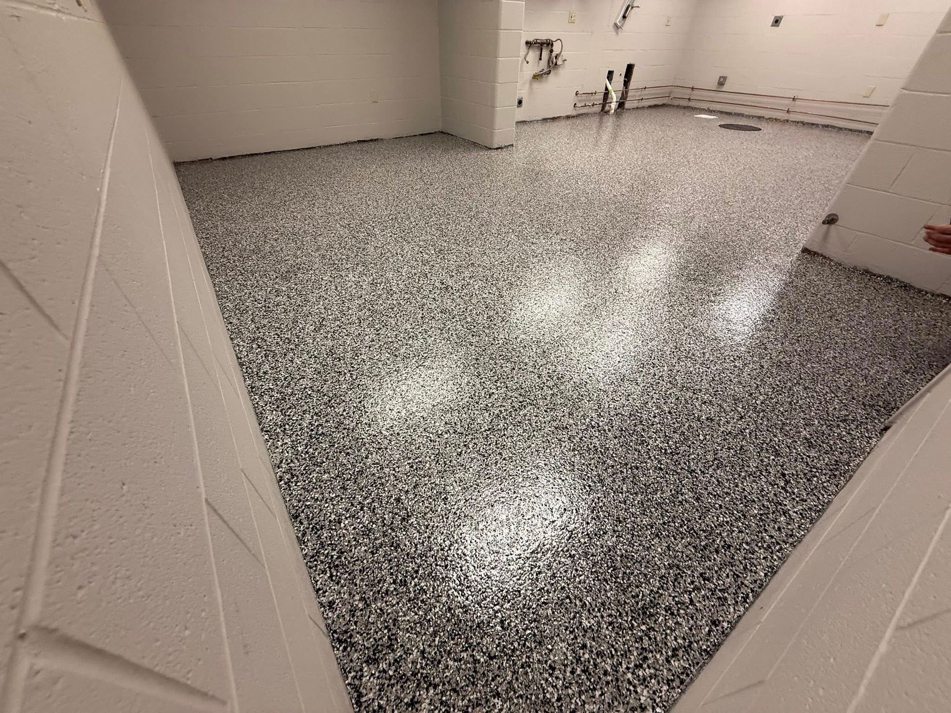 Epoxy-coated floor in a room. Grey, speckled pattern. White walls. Construction or renovation setting.