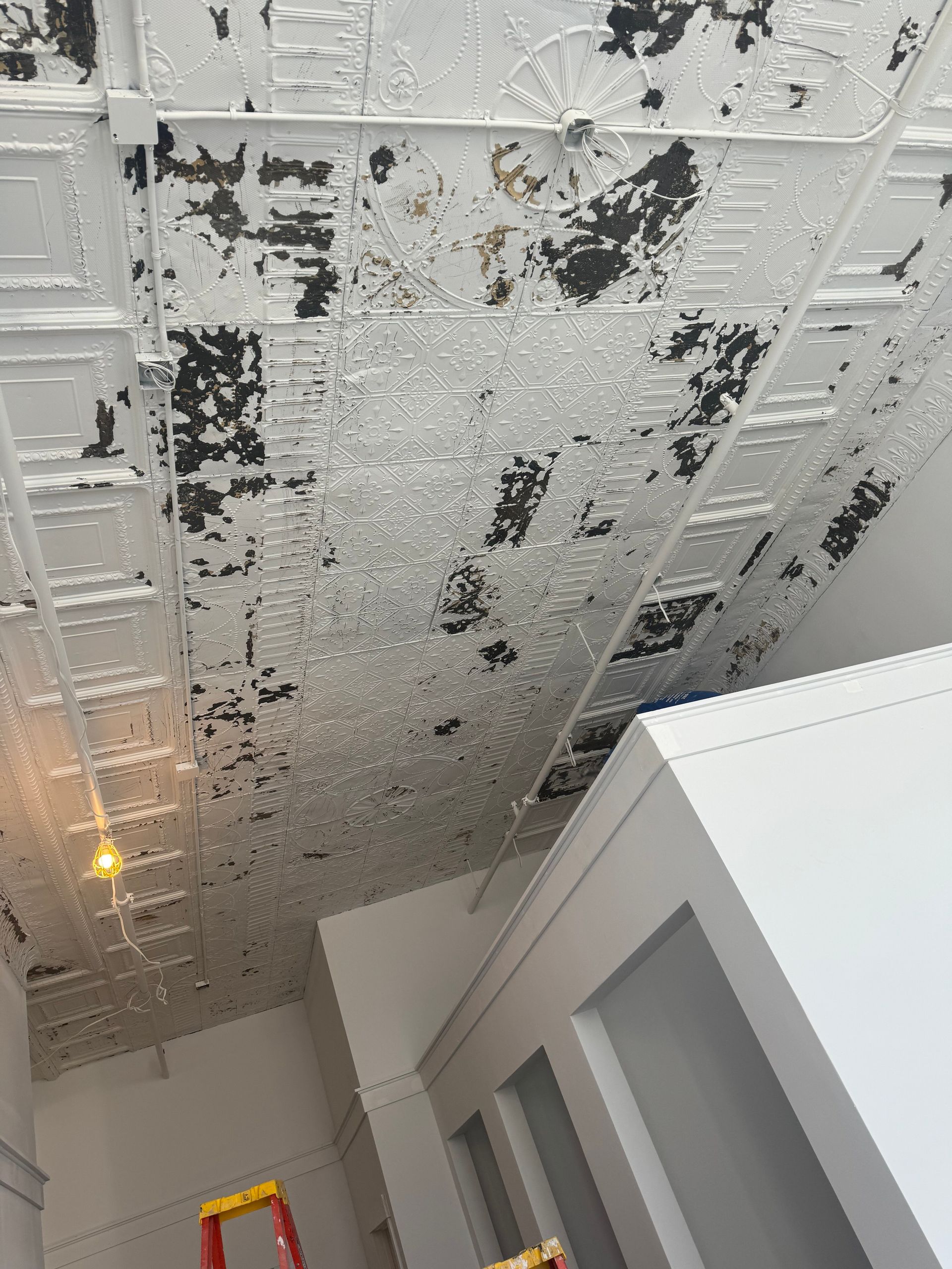 A white ceiling with black spots and a yellow ladder