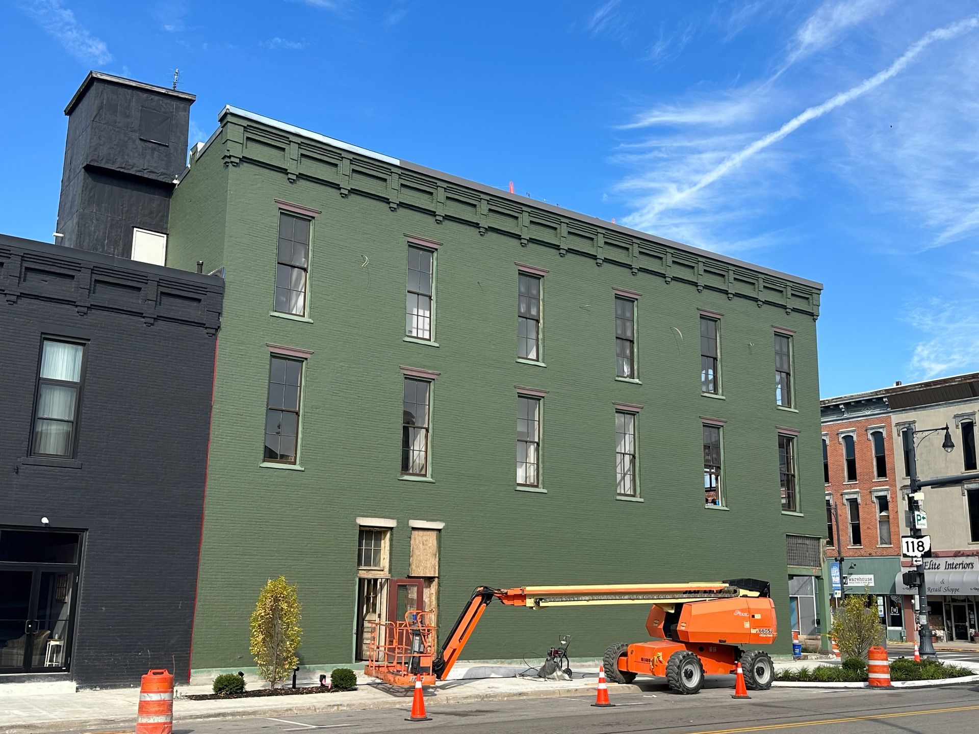 An orange crane is parked in front of a green building.