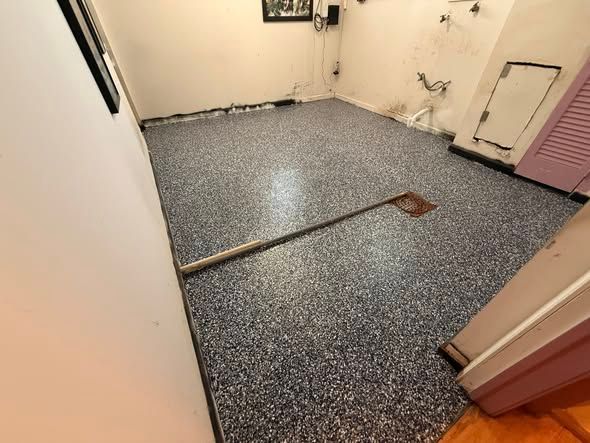 Room with dark speckled epoxy floor, a hoe, and white walls.