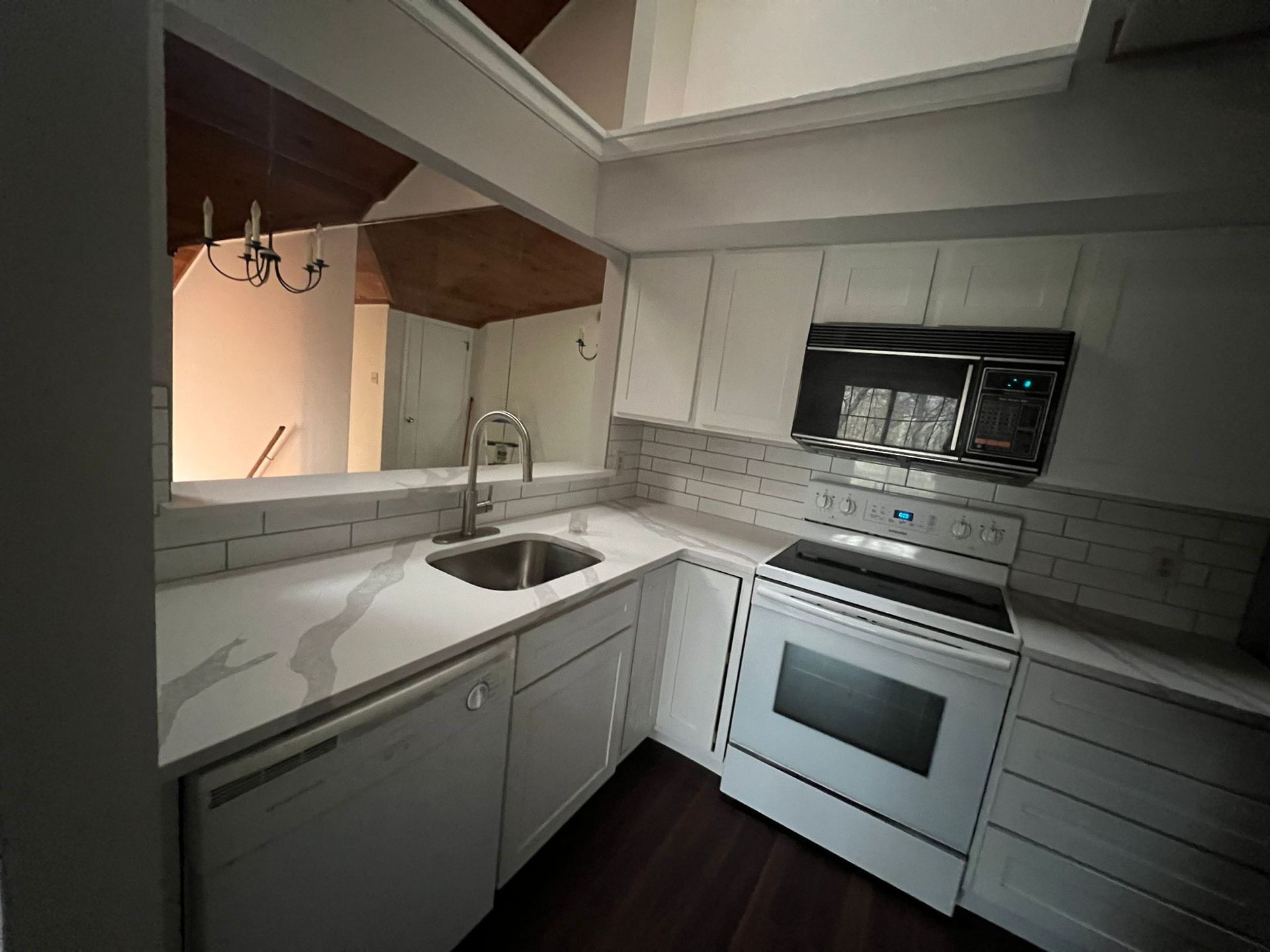 A kitchen with white cabinets , a sink , stove and microwave.