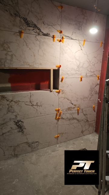 A bathroom with marble tiles being installed on the wall.