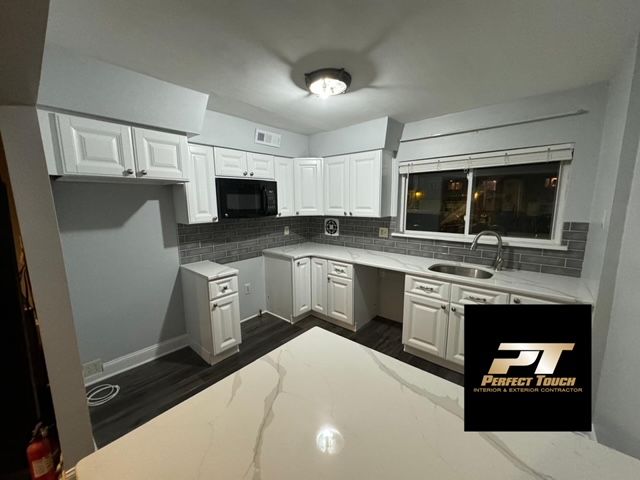 A kitchen with white cabinets , a sink , and a microwave.