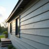 Side view of a house with blue-gray siding, dark window frames, and a wooden porch with steps.