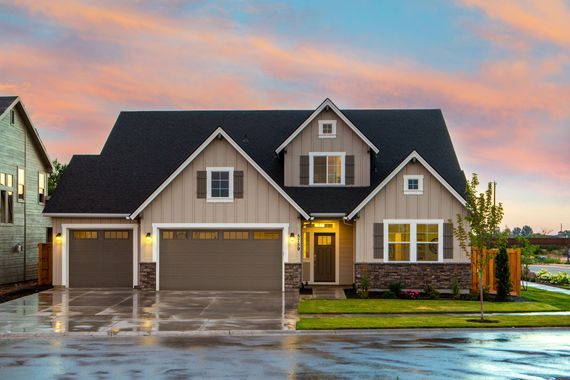 Tan and brown house with black roof; two-car garage, stone accents, and pink sunset sky.