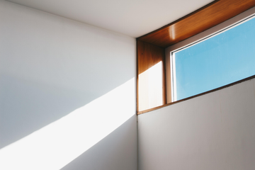 Sunlight on white walls, rectangular window with blue sky, wood frame.