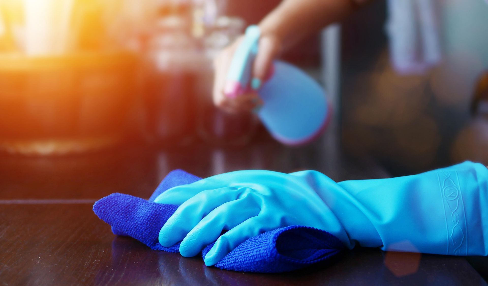 A person wearing blue gloves is cleaning a table with a cloth.