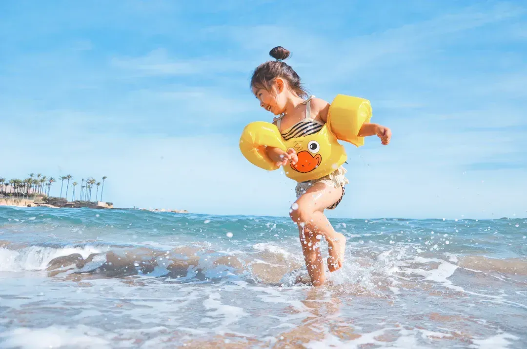 Young child wearing duck-themed floaties runs through ocean waves at the beach.