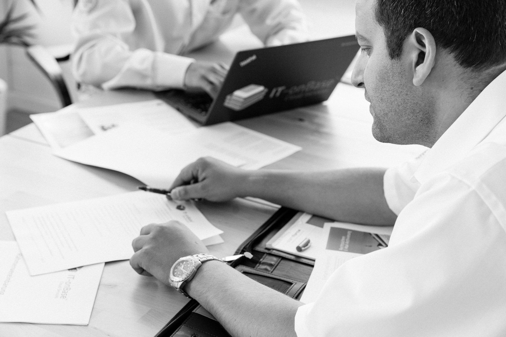 Ein Mann sitzt mit einem Laptop und Papieren an einem Tisch.