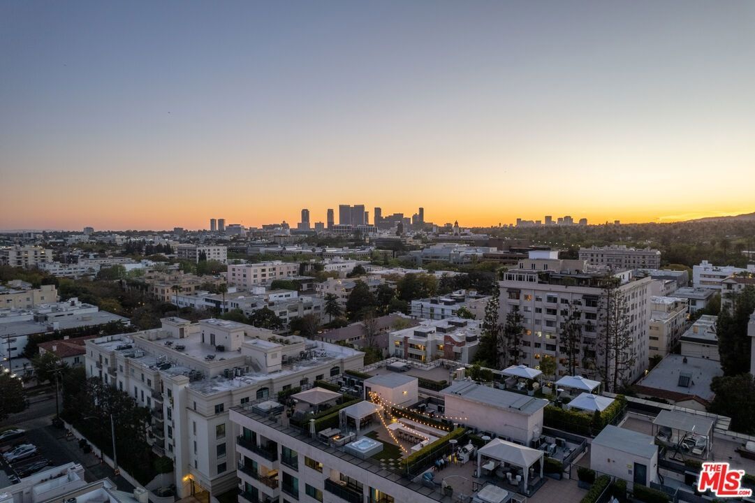 An aerial view of a city skyline at sunset, with low-rise buildings and residential rooftops in the foreground.