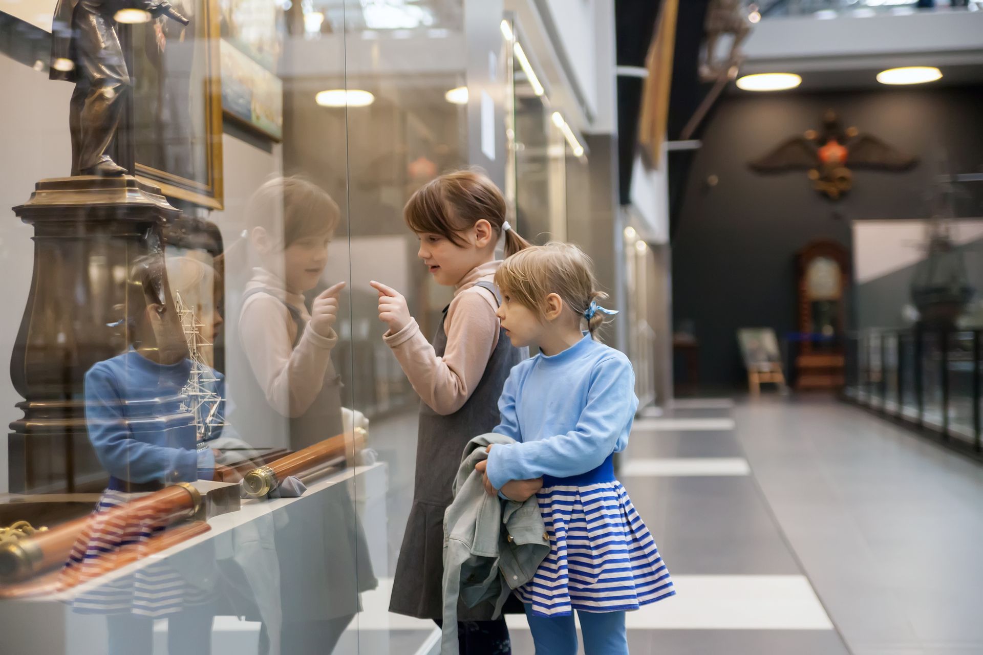A woman and a little girl are looking at a statue in a museum.