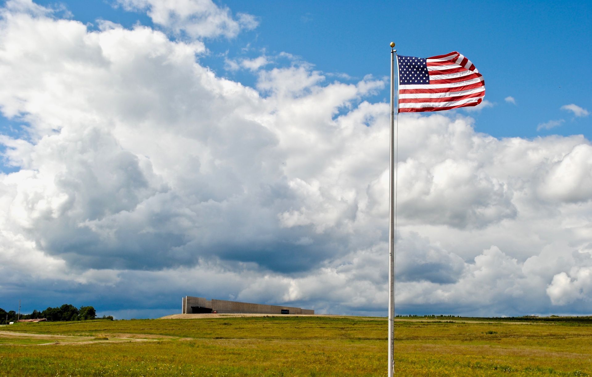 An american flag is waving in the wind in a field.