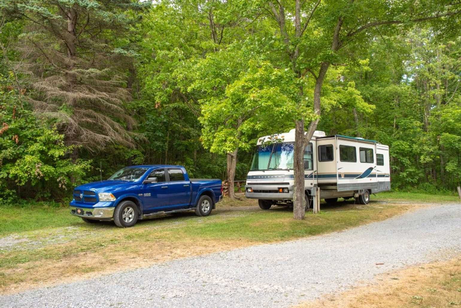 A blue truck is parked next to a rv in a campground.
