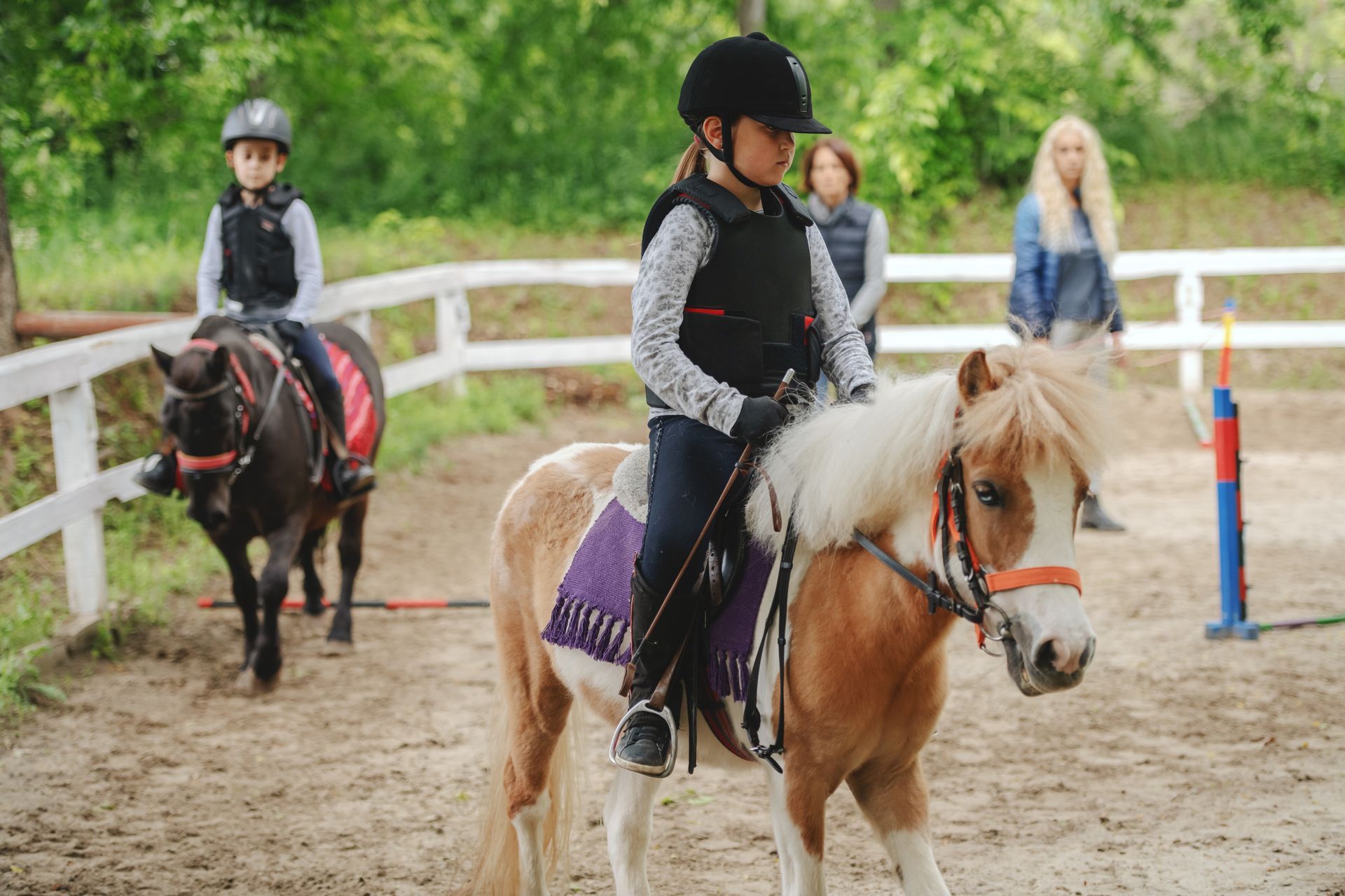 A young girl is riding a pony in a fenced in area.