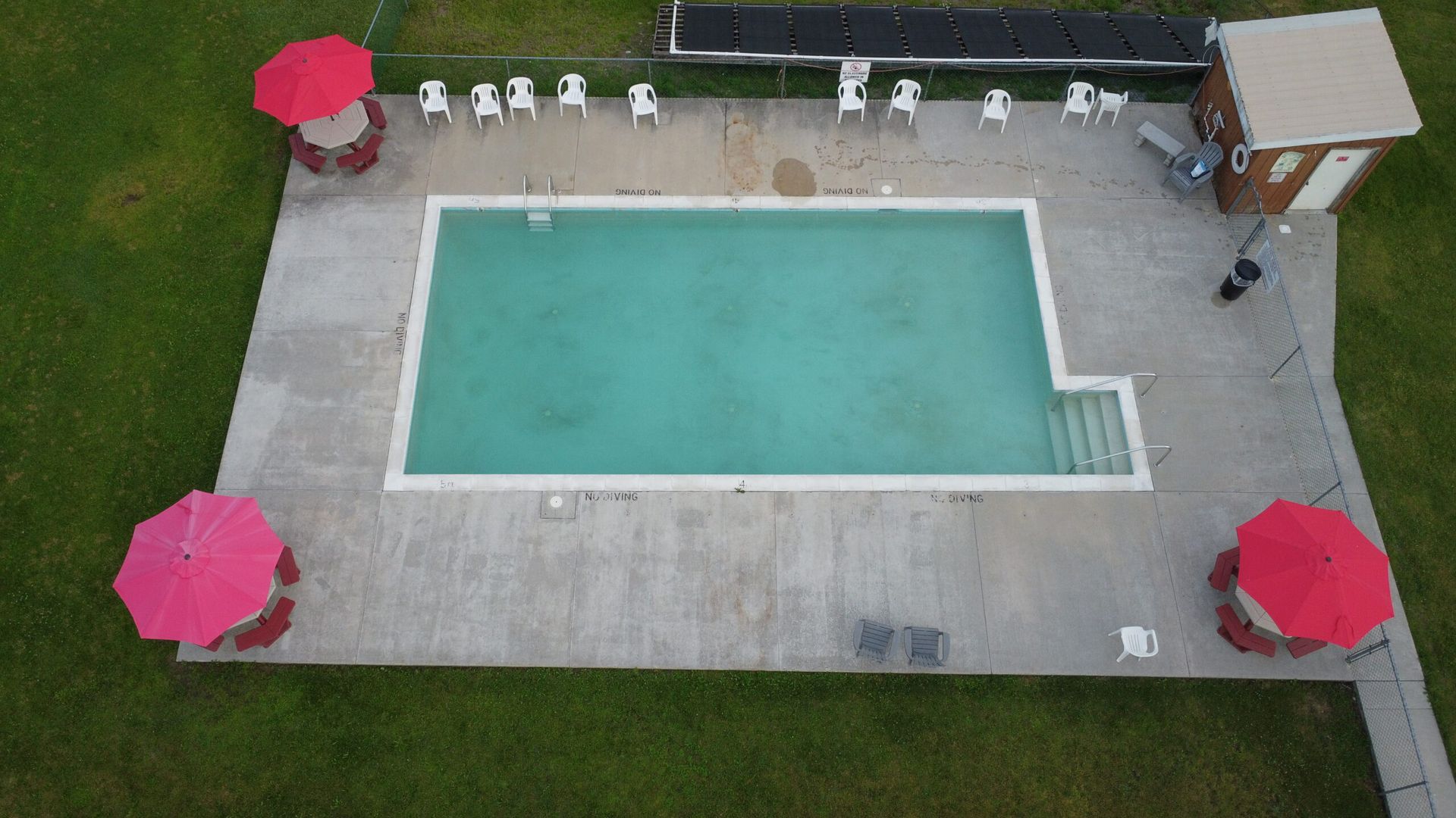An aerial view of a swimming pool with red umbrellas and chairs.