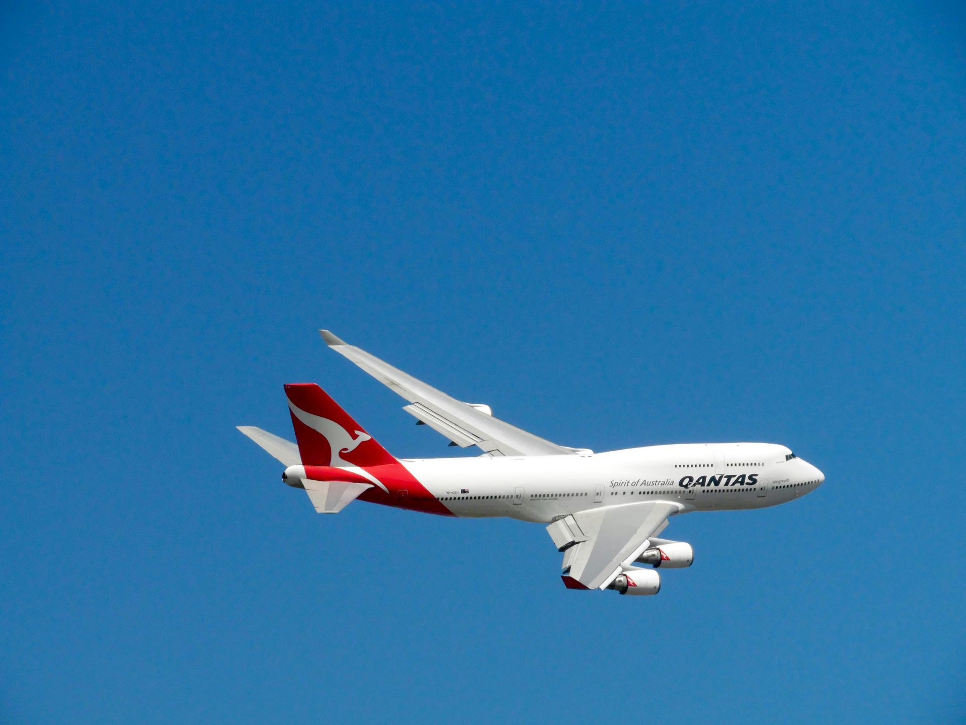 Qantas Boeing 747 airplane flying in clear blue sky. White fuselage with red tail and logo.