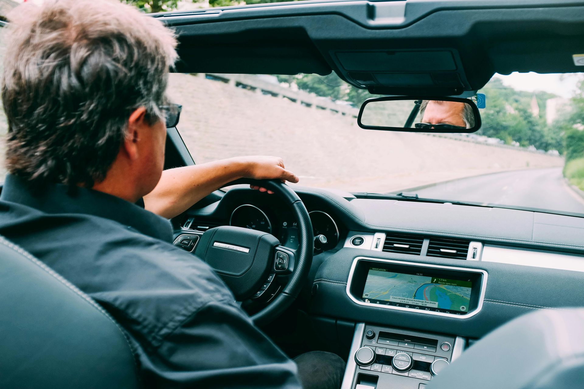 Man driving a convertible on a winding road. Interior view, steering wheel visible.