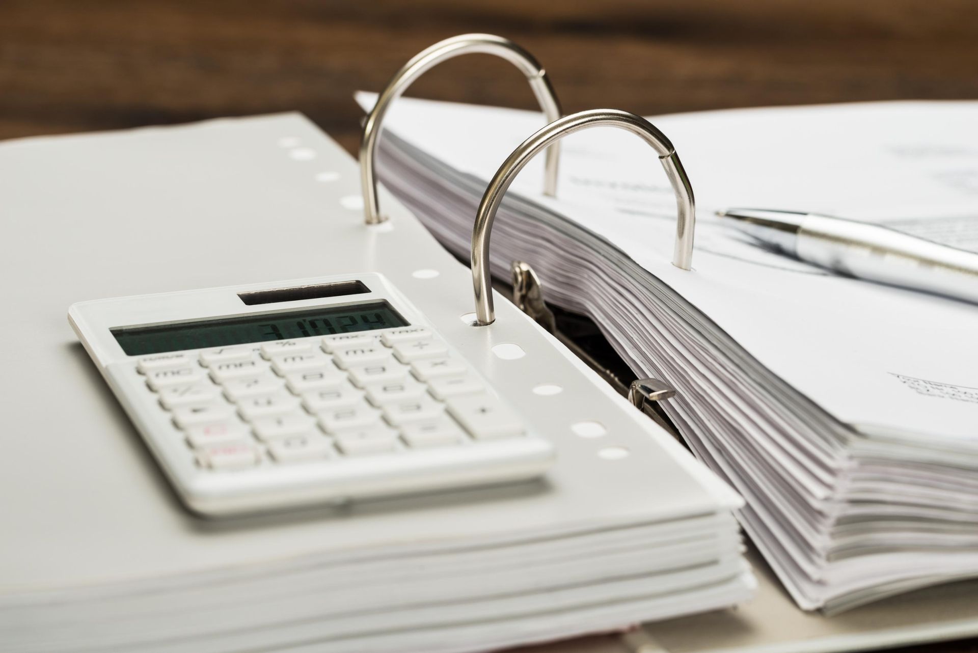 A calculator is sitting on top of a binder with papers and a pen.