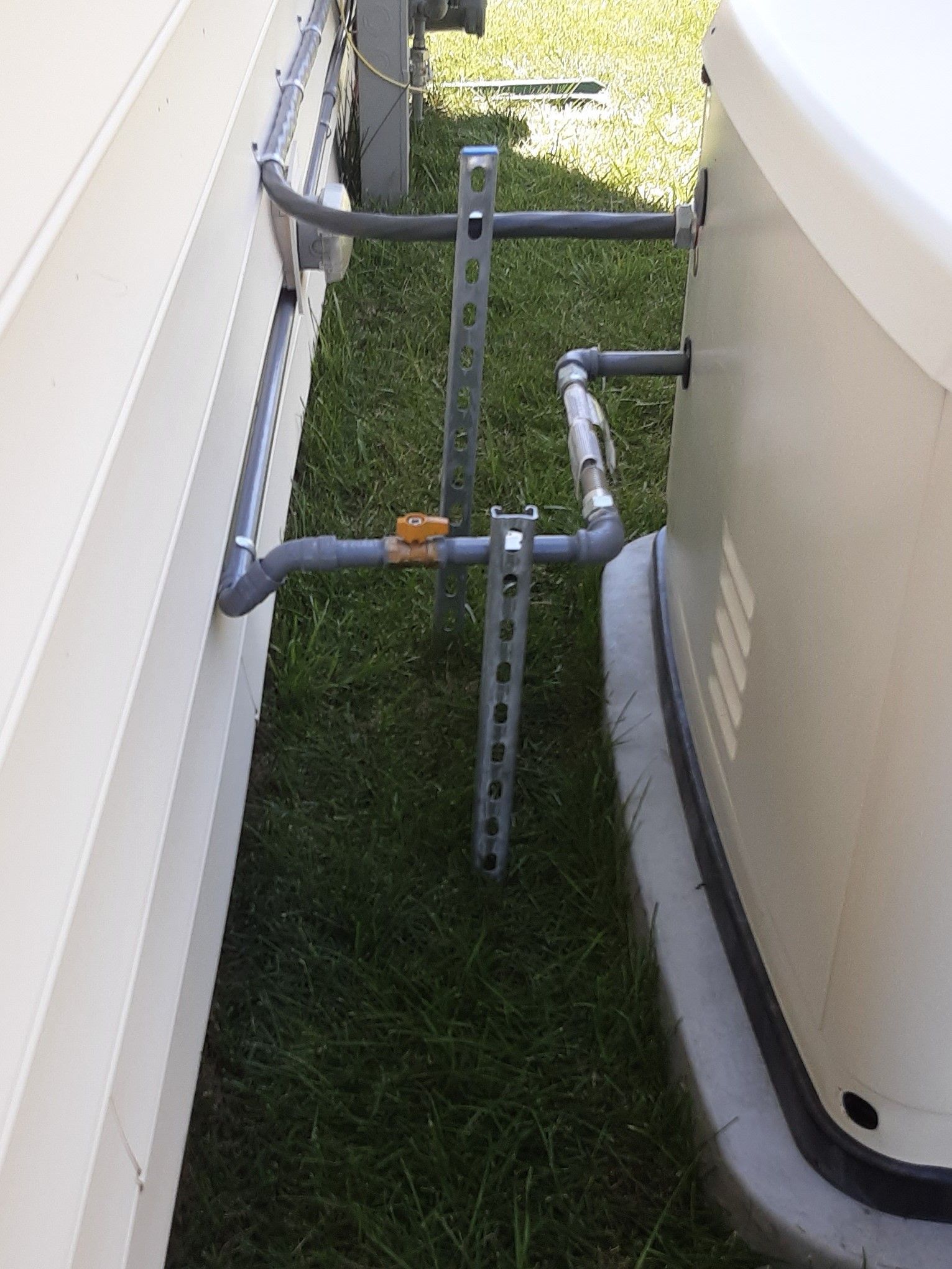 Piping with a valve and metal supports between two white structures on grass.