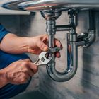 A plumber is fixing a sink pipe with a wrench.