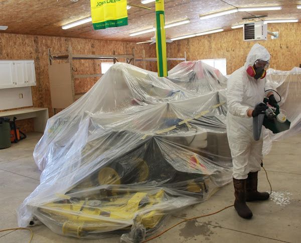 A man in a protective suit is spraying a john deere tractor