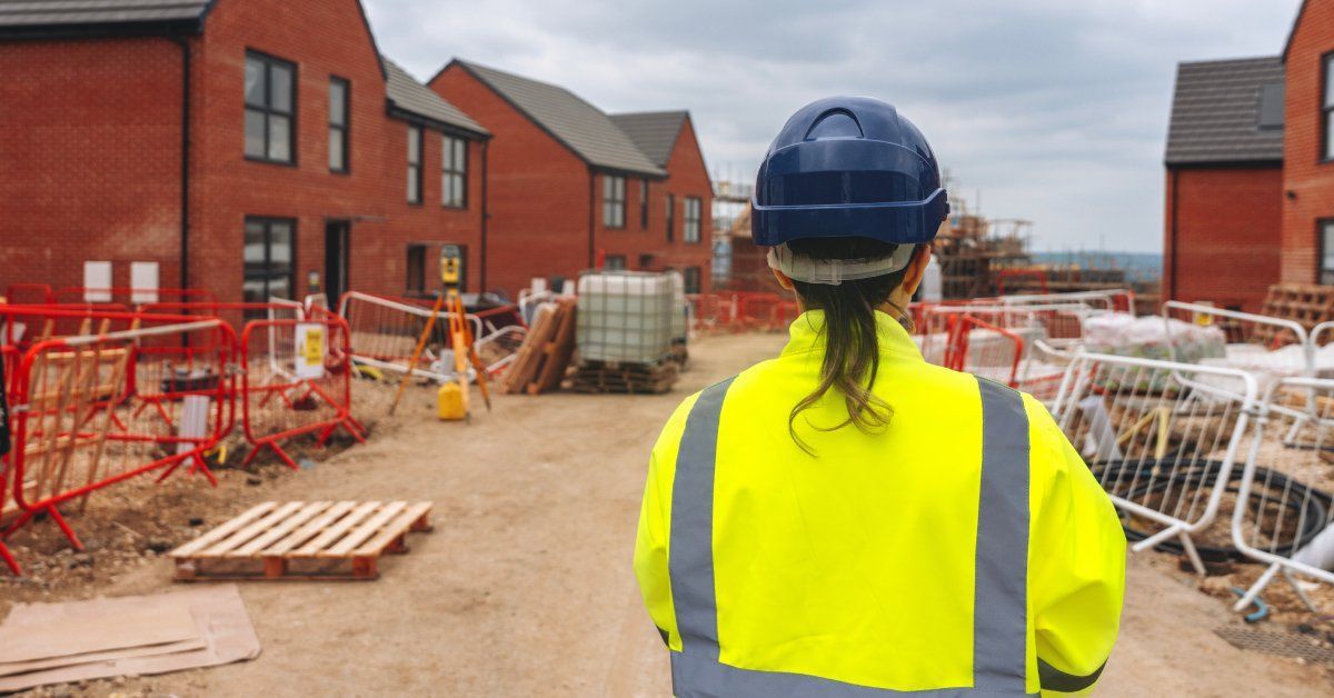 A construction worker is standing back to evaluate a block of vacant houses lined with equipment.
