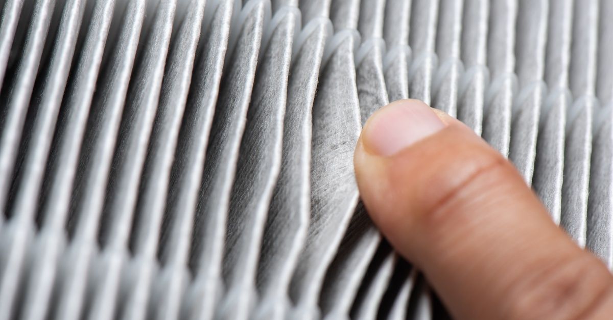 A close-up of the fabric pleats of a clean HEPA filter. A person's finger is pulling back the pleats