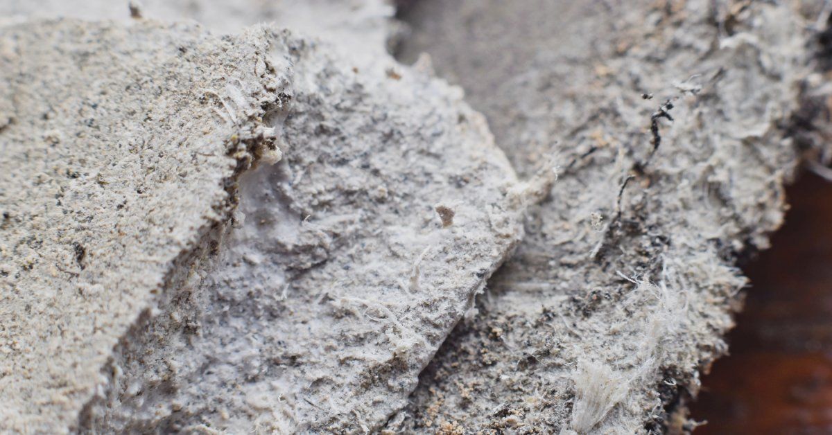 A close-up of thick sections of crusty housing materials overlapping, covered with dusty asbestos.