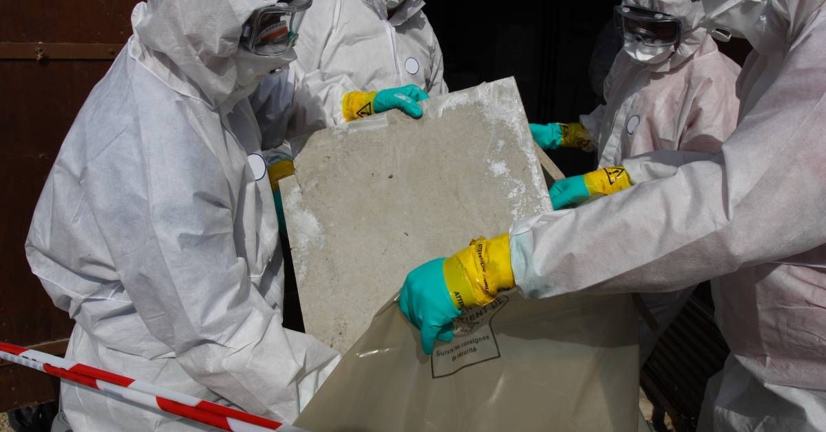 A team of workers in white hazmat suits are removing sheets of housing material with white asbestos 