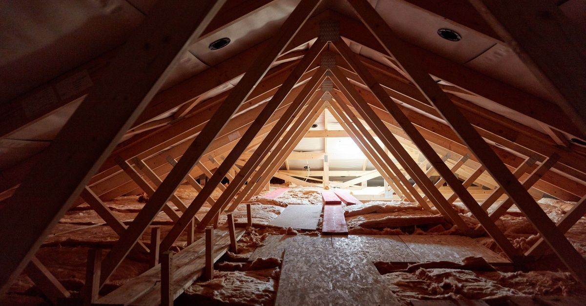 The interior of a small, unfinished attic. Patches of insulation are exposed, and light is coming in