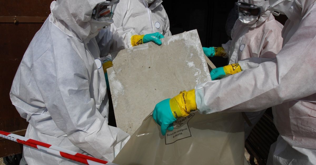 A team of professionals wearing protective gear handles material during an asbestos abatement.
