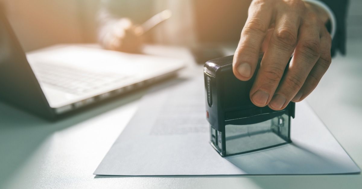 A close-up of a person wearing a suit using a stamp to validate a document.