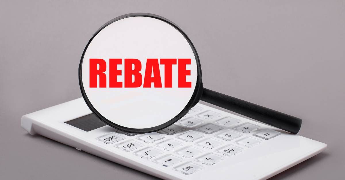 A black magnifying glass stands on a white calculator. The word “Rebate” is inside the magnifying gl