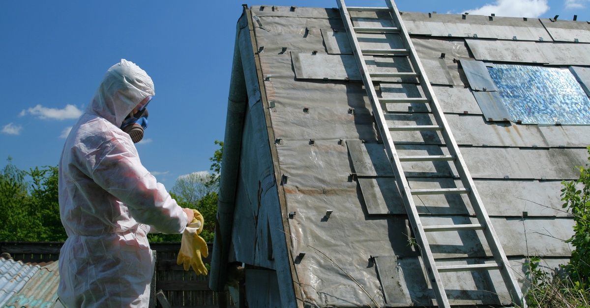 A person wearing full PPE stands in front of a house that is sealed for asbestos removal.